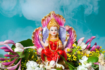 Hindu goddess Lakshmi. Statue and flowers with smoke on a blue background. 
