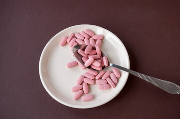 A plate with tablets and a spoon on a brown background