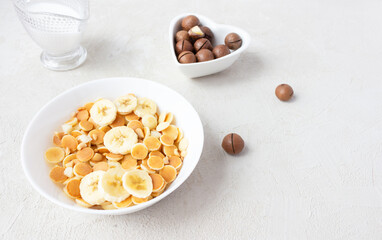 Mini pancakes with banana in a white cup with milk and macadamia nuts. Pancake flakes are the new trend of breakfast.