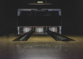 Leisure, entertainment and activities concept. Abstract background with copy space of old and dark parquet bowling track with white pins at the end of it. Floor in the center is in camera focus