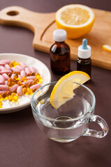 Tablets and fish oil in a plate and a transparent Cup with lemon on a brown background, cold and flu treatment