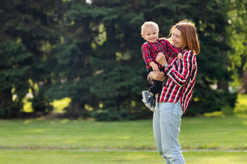 Fototapeta premium Cute cheerful baby with mother hug outdoors in park. Happiness and harmony of family life. Great family vacation. Mother and son have activities together on holidays.