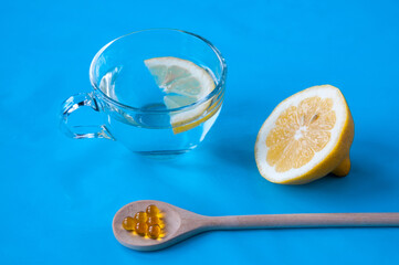 Wooden spoon with fish oil, cut lemon and a Cup with water and a slice of lemon on a blue background