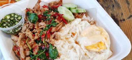 Close-up Fried organic chicken freshness basil with rice, slide cucumber and oily fried egg , seasoning spicy saltd fish sauce on ceramic plate at fusion gourmet cafe restaurant, food stylist backgrou