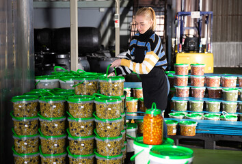 Positive woman working at the warehouse, stacking plastic containers with the selected olives
