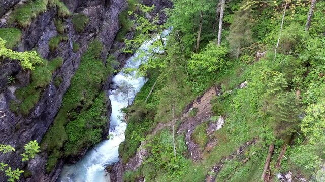 Steady aerial view of mountain river Partnach forcefully flowing through the canyon. It is surrounded by stone walls, moss and green trees