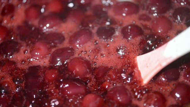 rack focus of cooking cherry fruit jam in a pot.