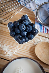 Vertical top view food ingredients for confectionery still life shot of blueberries on a wooden background with spoon, beater flour, coconut milk, strainer and kitchen towel with negative space. 