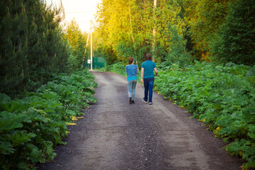 A man and a woman walk along a forest road towards the sun.