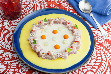 Traditional peruvian ceviche plate on a Chicha style tablecloth with cancha, prawn, corn, fish, sweet potato, napkins, spoon fork and a jar of beer. Gastronomy identity of the countryside of Peru