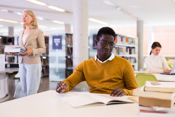 Fototapeta premium Intelligent african-american male student engaged in research working with books in university library