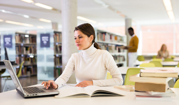 Portrait of smiling woman with laptop and book in public library