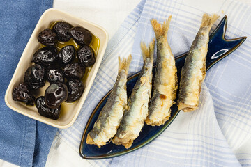 Spanish healthy omega 3 nutritious food mediterranean tapas starter concept with a fish shape plate with sardines and artisanal black olives and olive oil on a seafood themed blue table with napkins. 