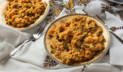 Food shot of plated Zaalouk with green olives. Typical mediterranean Moroccan salad starter with zucchini, onion, tomato, spices and egg on a traditional table cloth with forks, napkins and glasses. 