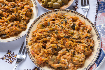 Food shot of plated Zaalouk with olive, napkins and forks. Moroccan salad starter  with zucchini, onion, tomato, spices and egg. Catering, traditional restaurant, weddings and family meeting concept