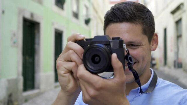 Happy cheerful young man taking pictures in old city street, holding and using dslr photo camera, smiling, laughing, talking to model. Closeup shot. Photographer concept