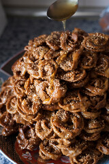 Vertical shot of a big size plate full of freshly fryed chebakia Moroccan sweets with a spoon topping the biscuits with a mix of honey and orange flower water. Ramadan food vertical stills.