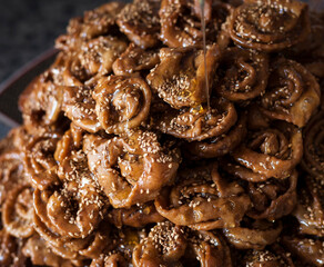 Vertical shot of a big size plate full of freshly fryed chebakia Moroccan sweets with a spoon topping the biscuits with a mix of honey and orange flower water. Ramadan food vertical stills.