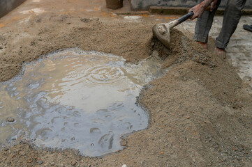 Indian labour mixing cement and water manually on floor using a shovel. Stock image.