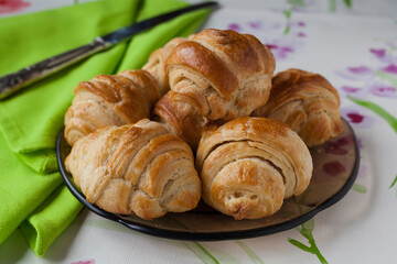 Food shot of homemade french croissants on a traditional plate with a green napkin, vintage knife and floral soft tablecloth with negative space.