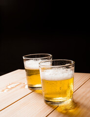 Vertical shot of two glasses of beer on a home wooden table with black background negative space. 