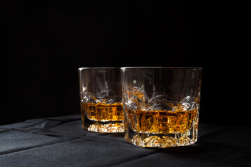 Two glasses of scotch whiskey on a black tablecloth with black background negative space. Hard alcoholic drinks and elegant night life concept.