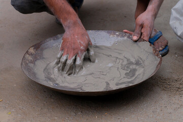 Indian labour mixing cement and water manually on bucket using bare hands. Stcok image.