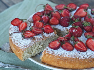 Spring berry cake with strawberries at the top on a wooden background.