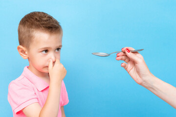 Little boy clamps his nose with his hand and refuses to drink medicine
