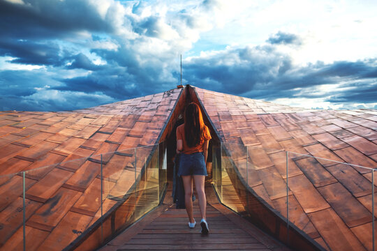 Rear view image of a young woman traveling and walking into a modern wooden building