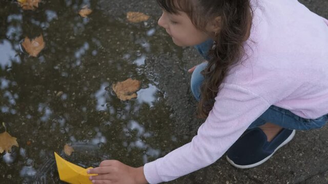 Girl with paper ship. A cute little girl is playing with a paper boat in a puddle of autumn leaves.