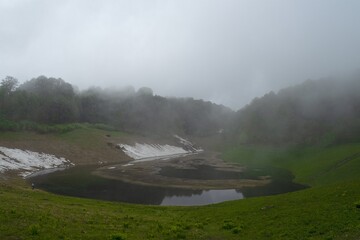 Alpine lake at the top of the mountain. Cloudy spring day. Remains of snow on the banks. Fog forms above the water and the forest. Pure nature.