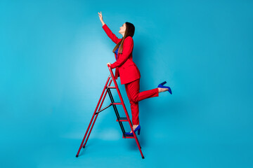 Full length profile photo of professional fancy lady worker come up career ladder touch success with arm wear luxury red suit blazer pants high-heels isolated blue color background © deagreez