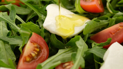 pouring olive oil on arugula salad with tomatoes and mozzarella cheese. top view