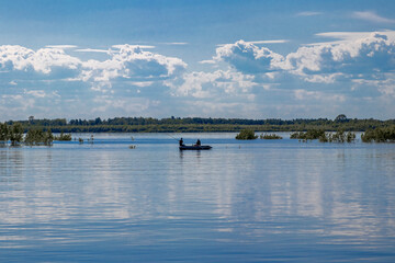 Landscape. River. There are clouds in the sky. River boat with fishermen.