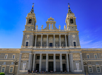 Fototapeta na wymiar Main facade of the Cathedral of Our Lady of La Almudena by the Royal Palace, people sitting on steps in Madrid, Spain