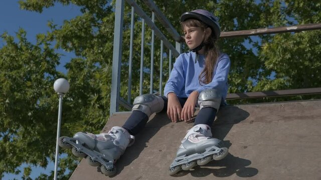 City roller rink. A teenage girl sits on a rollerdrome in a helmet and rollers.