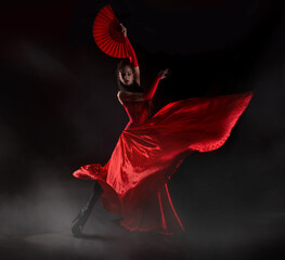 Flamenco woman spanish dancer in red dres performs with fan in dance at black background, studio shot - obrazy, fototapety, plakaty