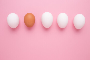 The concept of personality. Brown egg among white eggs on a pink background.
