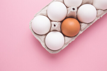 Tray with chicken eggs on a pink background. A brown egg among white. The concept of individuality.