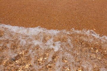 Fototapeta na wymiar Sea background. Sand texture. A wave floating on the sand closeup. 