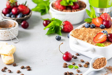 Classic Italian dessert Tiramisu decorated with strawberries, cherries and mint on a white background.