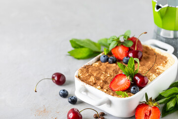 Classic Italian dessert Tiramisu decorated with strawberries, cherries and mint on a white background. Copy space for your text.