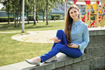 Universal concept on a background of trees. Portrait of caucasian brunette girl in the park with smile in sunny weather.