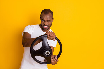 Photo of attractive dark skin guy man trying hard to turn car left right holding steering wheel driver wear casual white t-shirt isolated yellow vibrant color background - Powered by Adobe