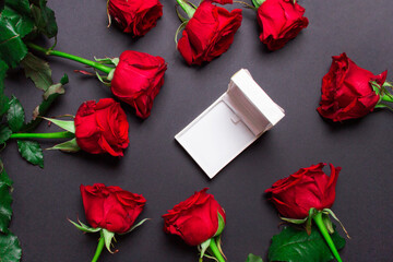 Red roses and white open jewelery box on black colored paper background , top view