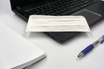 Laptop, surgical face mask and pen over white background