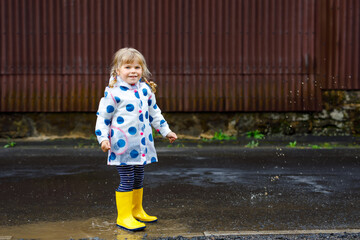 Little toddler girl wearing yellow rain boots, running and walking during sleet on rainy cloudy...