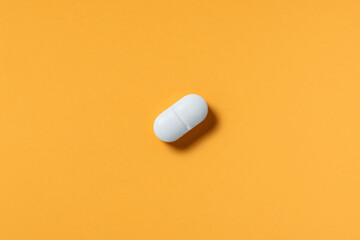 White pill or capsule lies on orange background top view copy space