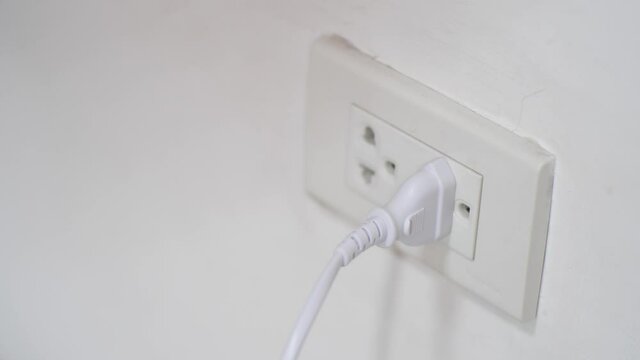 Closeup of hand inserting an electrical plug into a wall socket.